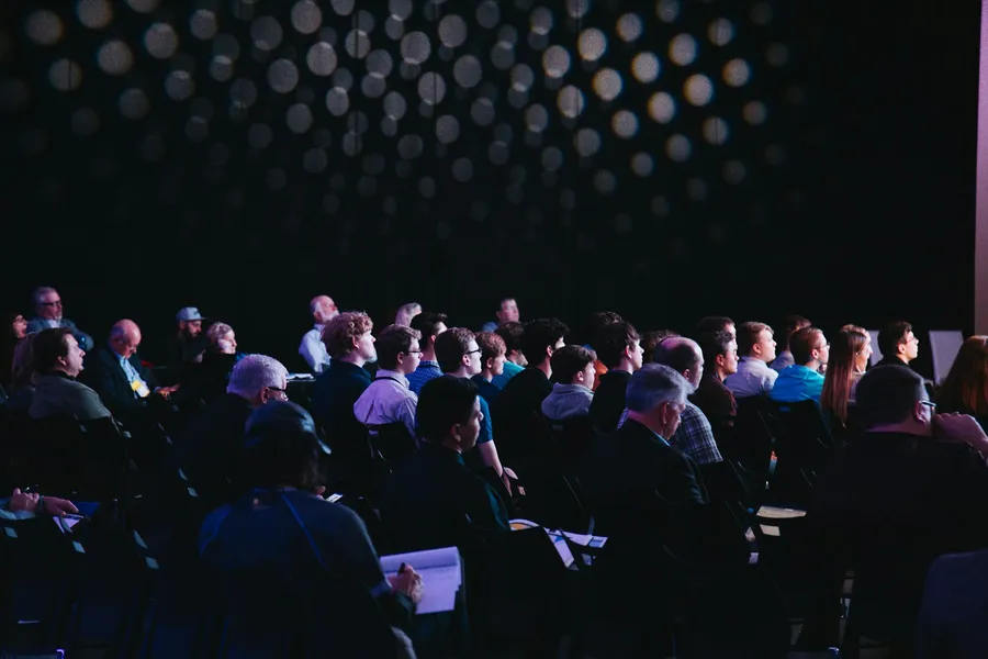 An audience seated in a darkened auditorium, facing a stage